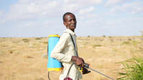 Man standing with pesticide spray in front of arid landscape