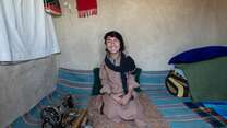 Darweza sits smiling at home beside his sewing machine.