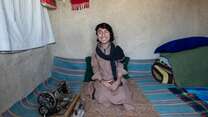 Darweza sits smiling at home beside his sewing machine.