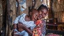 A mother holds her young child close as the two share a smile while playing.