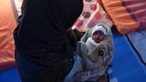 Alina and her infant daughter sit on the floor of a tent in a refugee camp in Iraq