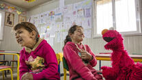 Elmo, the Sesame Street Muppet, makes two Syrian refugee girls laugh