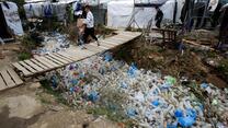 Man walking on wooden bridge under which are many discarded plastic bottles 