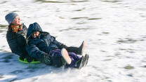 An IRC mentor sleds down a hill with a boy resettled from Somalia