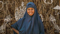 Nurta is smiling at the camera. Her drawings are displayed in the image behind her.