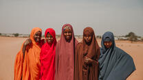 Five girls dressed in bright colours smile at the camera.