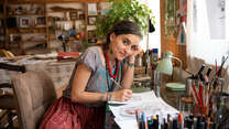 Artist Diala looks up at the camera from her desk where she is designing the IRC's WRD illustration.