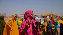 Zainab dressed in pink speaks into a megaphone in front of a crowd of people in Helowyn camp in Ethiopia. 