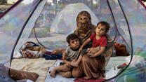 A woman holds her two children as they sit inside a tent