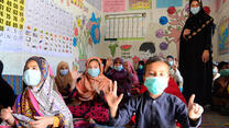 A female teacher in Pakistan with a group of children in a class room all wearing masks