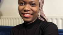 Fatou Jeng climate activist smiles at the camera in front of a blue and white background