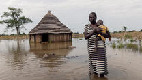 Abuk stands with her daughter outside her flooded home in South Sudan.