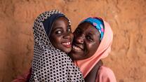 A smiling 8-year-old Nigerian girl, Fatima, hugs her smiling mother in Nigeria before she heads to school.