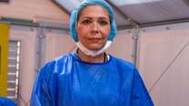 Dr. Edna, an IRC doctor from Venezuela working in Colombia, is inside a medical tent and wearing bright blue scrubs. She is looking straight at the camera. 