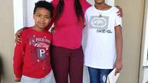 Abrehet stands with her arms around her children Kudus, 5, and Delina, 8, outside their home.
