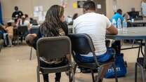 In the IRC's Welcome Center for asylum seekers, a husband and wife sit with their back to the camera as they discuss their journey as asylum seekers. The wife is holding their 2-year-old daughter. 
