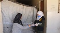 A woman signs a form offered by a female IRC aid worker wearing a mask as a COVID-19 precaution while distributing emergency cash assistance.