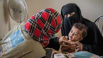 An IRC health worker examines a child in Yemen for malnutrition as his mother holds him in her arms.