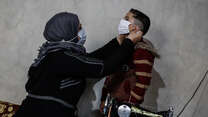 Um Abdo fits a COVID-19 face mask she's sewn on her son.