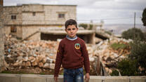 Ten-year-old Ali stands in front of his family's home which was damaged by an airstrike. 