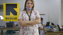 Dr. Edna Patricia Gomez stands in scrubs with her arms crossed. She has mask at her chin and there is an IRC logo behind her. 