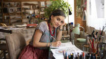 Artist and activist Diala Brisly, leaning on her desk holding a pencil, sketches an illustration of refugees for World Refugee Day 2021.