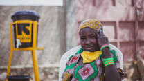 Ten-year old Anastasie sits elbow leaning on chair near an IRC hand-washing station, her COVID-19  face mask pulled down around her neck.