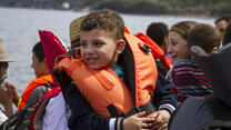 A child in a lifejacket with other refugees in a raft approaching a Greek beach 