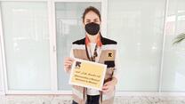 Fatima, a home visiting officer for the IRC in Mexico, holds a sign that says "welcome to Mexico" in English, Spanish and Dari. She is wearing a mask and an IRC vest. 