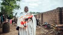 A Nigerian mother smiles and holds her baby who is wrapped in a blanket.