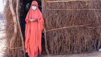 teacher Misra Hussein Ahmed wears a COVID-19 face mask while standing outside her temporary classroom made of branches in an Ethiopian displacement camp.