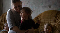 A mother sits holding one of her sons on her lap. Two other children sit in chairs behind them. 