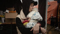 A Ukrainian mother in winter clothes holds her bundled-up baby at a Ukraine-Poland border crossing point.