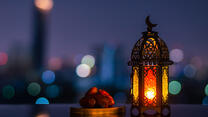 A lantern that has moon symbol on top and small plate of dates fruit with night sky and city bokeh light background for the Muslim feast of the holy month of Ramadan.