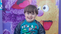 Saeed, a 5-year-old Syrian boy born with Down's Syndrome, stands in front of a poster with Sesame Street characters.