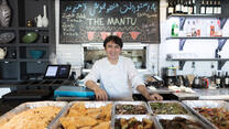 An Afghan chef smiles as he stands near trays of food at his resturant in Virginia