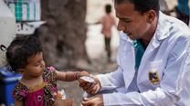 An IRC nutritionist crouches on the ground to give a young girl a packet of peanut paste when his IRC mobile health team visits her village in Yemen.
