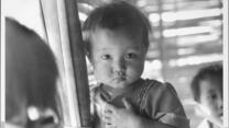 A young girl from Southeast Asia looks at the camera with a serious expression.