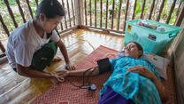 An IRC health worker takes the blood pressure of a female patient lying on a mat on the floor in Thailand.