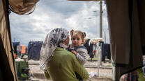 A mother holds her toddler daughter and looks out from their tent on a cloudy day in a refugee camp in Idomeni, Greece.