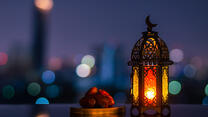 Lantern that have moon symbol on top and small plate of dates fruit with night sky and city bokeh light background for the Muslim feast of the holy month of Ramadan Kareem.