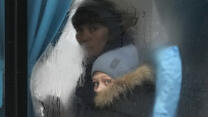 The smudged window of a bus with a woman and child peering out of it. They are wearing winter hats and coats. 
