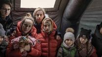 Women and children from Ukraine, stand inside a tent wearing winter clothes inside a tent
