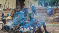 Three women and two children from CAR sit around a fireplace in a camp for displaced people.