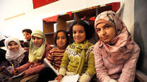 Five Syrian girls sitting in a school in Lebanon holding papers and pencils.
