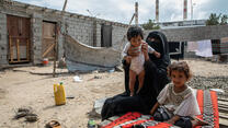 A mother and her two young children seated outdoors in Yemen