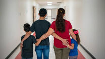 Luisa, an asylum seeker from Mexico, stands with with her children in Arizona after she was able to cross the US border. They are standing in a hallway with their backs to the camera, to protect their identities. 