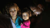 A mother holding her young daughter claiming asylum with two border control agents.