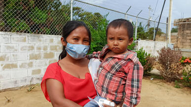 A mother holds her son and the pair pose for a photo outdoors.