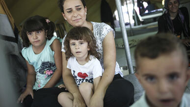 A Syrian refugee woman sits with her son and other family members inside a tent.